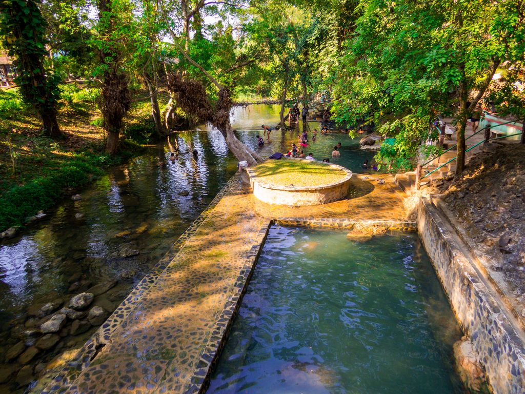 People at the Hhe Hin Dat hot springs surrounded by trees in Kanchanaburi, Thailand.